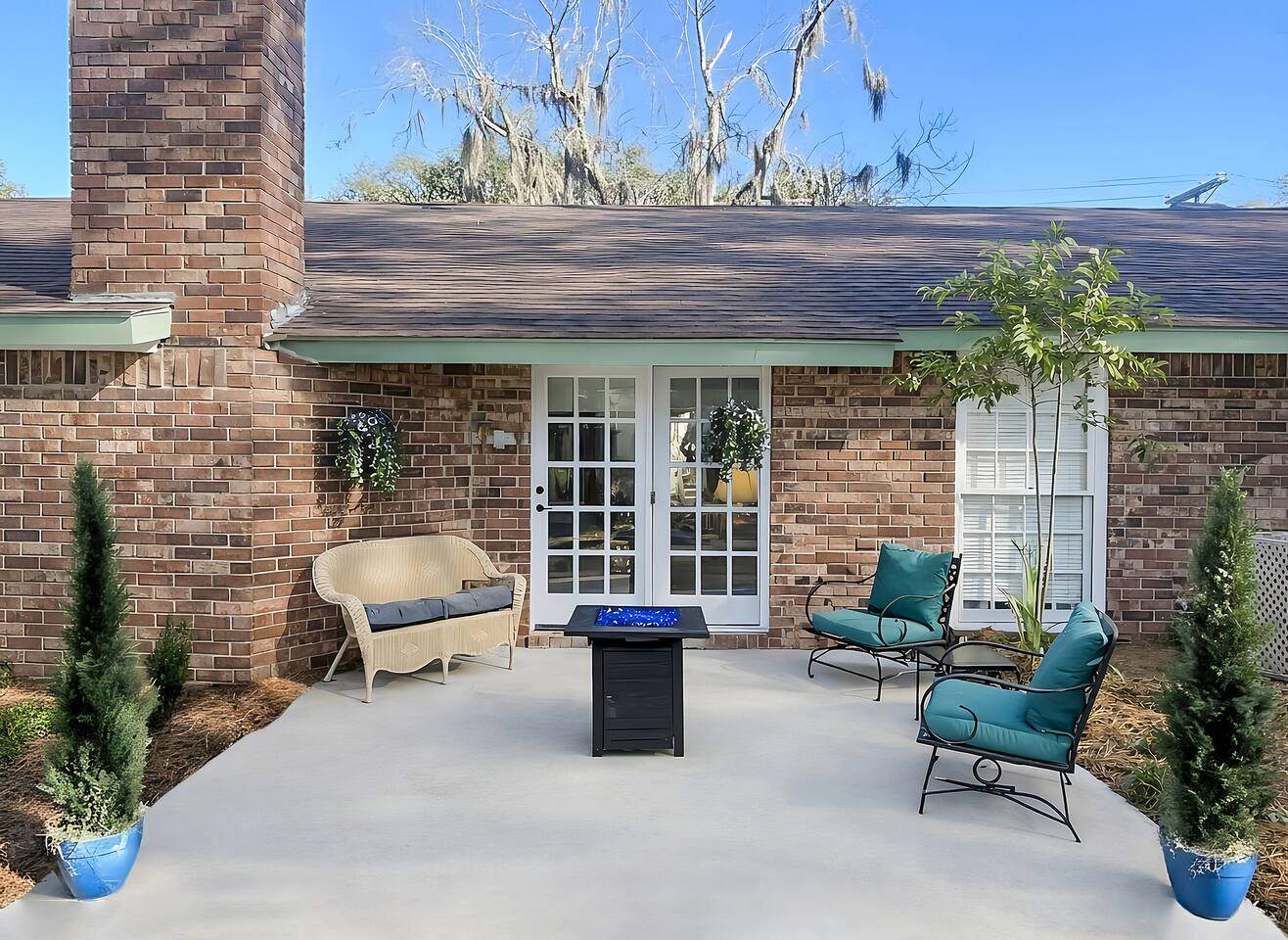 Brick back patio with fire table and lounge chairs under live oaks draped in Spanish moss